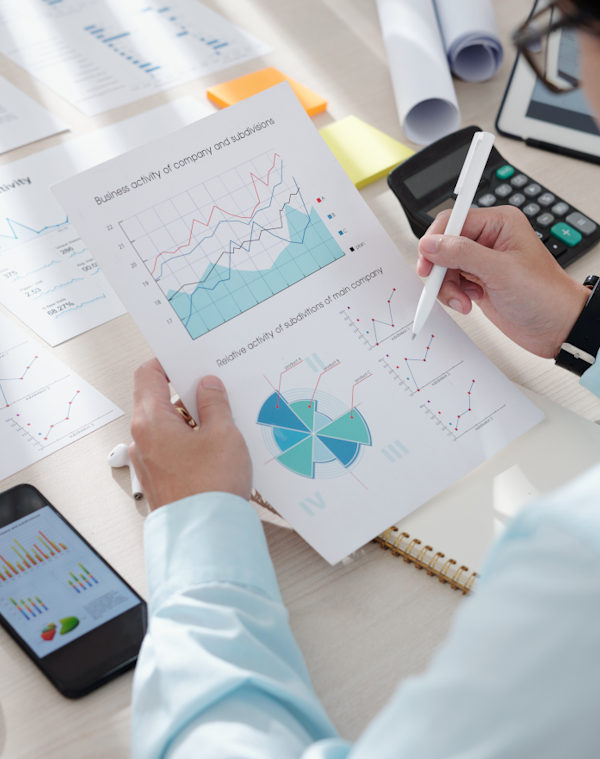 Photo of man arms resting on a desk, holding a financial report, with calculator and mobile phone on the desk.